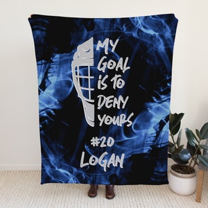 May include: Blue and black fleece blanket with a hockey mask graphic and the text "My goal is to deny yours #20 Logan".