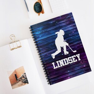 Könnte beinhalten: Ein Spiralblock mit einem Galaxie-Design, das eine weiße Silhouette eines Hockeyspielers zeigt. Der Name "Lindsey" ist in weißen Buchstaben auf dem Cover gedruckt.