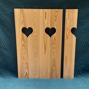 May include: Three wooden panels with heart-shaped cutouts. The panels are light brown and have a natural wood grain. The heart cutouts are black.