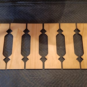 May include: Six unfinished wooden decorative panels with a light brown color. Each panel has a unique cutout design, featuring a series of vertical shapes with diamond and rectangular cutouts. The panels are arranged on a dark surface.