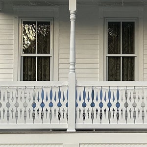 May include: A white wooden porch with two windows and a white picket fence with a decorative design. The fence has a cutout pattern that resembles a series of teardrops.