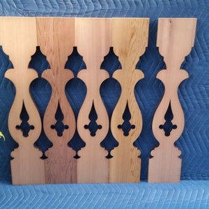 May include: Five unfinished wooden balusters with a decorative cut-out design. The balusters are arranged in a row on a blue surface.