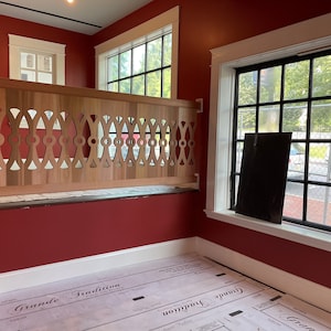 May include: A red room with two windows, one with a black frame and the other with a white frame. The room has a wooden railing with a decorative design. The floor is covered with a white sheet with the words "Grande Tradition" printed on it.
