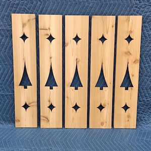 May include: Five rectangular light brown cedar wood planks, each featuring a vertical cutout design consisting of a central pine tree shape flanked by a four-pointed star shape above and below the tree, showcasing natural wood grain and knots.