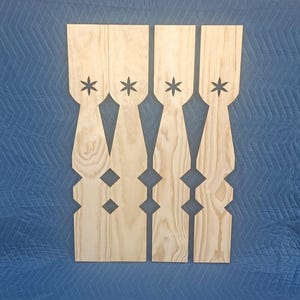 May include: Four vertical light-colored wooden balusters featuring a natural wood grain pattern. Each baluster has a flat top, a cutout six-pointed star shape near the top, and a decorative, symmetrical silhouette with angular cutouts along the sides.