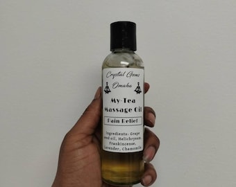Puede incluir: Una botella de vidrio transparente con una tapa negra y una etiqueta blanca. La etiqueta dice "Crystal Gems Omaha My-Tea Massage Oil Pain Relief" y enumera los ingredientes: aceite de semilla de uva, helichrysum, incienso, lavanda, manzanilla.