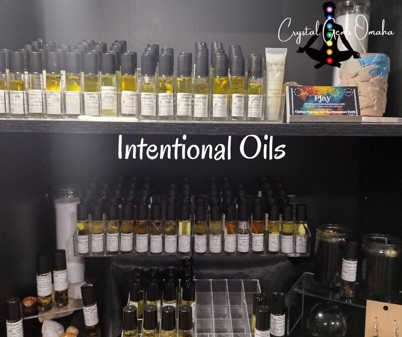 Puede incluir: Un estante de exhibici&oacute;n con peque&ntilde;as botellas de vidrio llenas de l&iacute;quido amarillo, etiquetadas como "Intentional Oils". Las botellas est&aacute;n dispuestas en filas en un estante negro. Las botellas son todas del mismo tama&ntilde;o y forma, y tienen tapas negras. El estante est&aacute; en una tienda con otros art&iacute;culos en exhibici&oacute;n.