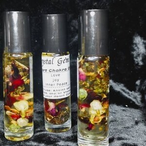 Puede incluir: Tres botellas de vidrio con rodillo llenas de un l&iacute;quido transparente y varias flores y hierbas secas. Las botellas est&aacute;n etiquetadas con "Crystal Gem's Heart Chakra Oil", "Love", "Joy", "Inner Peace", "Use: Anoint self and/or stones on your Heart Chakra"