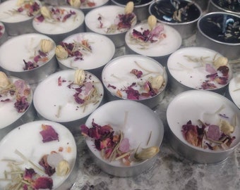 Puede incluir: Surtido de velas de té blancas con flores y hierbas secas. Las velas están en un recipiente plateado y están dispuestas en forma circular.