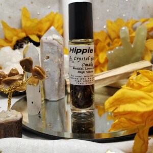 Puede incluir: Una peque&ntilde;a botella de vidrio con una tapa negra y una etiqueta blanca que dice "Hippie Crystal Grid Omaha Peace, Love & High Vibes To use: Aneint/ Makras etc to all high vibes are tree thinking". La botella est&aacute; llena de un l&iacute;quido transparente y algunas hierbas. La botella est&aacute; sentada sobre una superficie de espejo con un pa&ntilde;o blanco debajo.