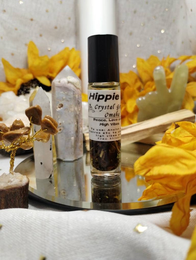 Puede incluir: Una peque&ntilde;a botella de vidrio con una tapa negra y una etiqueta blanca que dice "Hippie Crystal Grid Omaha Peace, Love & High Vibes To use: Aneint/ Makras etc to all high vibes are tree thinking". La botella est&aacute; llena de un l&iacute;quido transparente y algunas hierbas. La botella est&aacute; sentada sobre una superficie de espejo con un pa&ntilde;o blanco debajo.