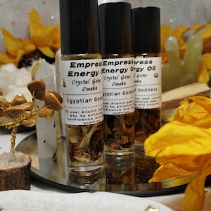 Puede incluir: Tres peque&ntilde;os frascos de vidrio con tapas de rodillo llenos de un l&iacute;quido marr&oacute;n. Los frascos est&aacute;n etiquetados con "Empress Energy Oil" con el texto "Crystal Gems Omaha" y "Egyptian Goddess".