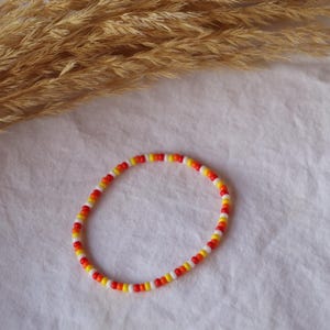 May include: A white, red, and yellow beaded necklace. The necklace is made of small, round beads that are strung together in a repeating pattern.