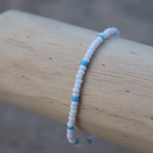 May include: A white beaded bracelet with small blue beads interspersed throughout.