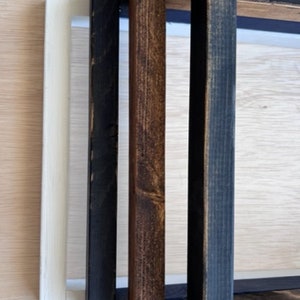 May include: Three wooden picture frames in different sizes and colors. The largest frame is black, the middle frame is brown, and the smallest frame is white.