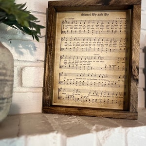 Puede incluir: Una impresi&oacute;n de partitura vintage enmarcada con el t&iacute;tulo "Sweet By and By" y la letra de la canci&oacute;n. La partitura est&aacute; impresa en papel envejecido con un fondo marr&oacute;n y notas musicales negras.