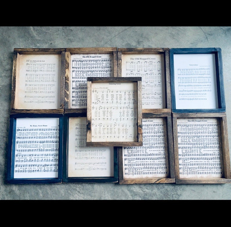 Puede incluir: Nueve piezas de m&uacute;sica en partituras enmarcadas con diferentes t&iacute;tulos de canciones, incluyendo "The Old Rugged Cross", "Amazing Grace" y "My Jesus, I Love Thee". Los marcos son de madera con un acabado r&uacute;stico y tienen un fondo negro o marr&oacute;n.
