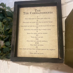 May include: A framed print of the Ten Commandments in a black frame. The text is in a traditional font and includes the Roman numeral for each commandment.