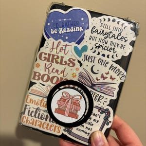 May include: A clear phone case with a variety of colorful stickers. The stickers feature book-themed quotes and illustrations, including "I'd Rather Be Reading", "Hot Girls Read Books", "Still Into Fairytales But Now They're Spicier", and "Just One More Chapter".