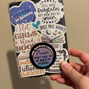 May include: A clear phone case with various colorful stickers featuring quotes about reading. The stickers include "I'd rather be reading", "Hot girls read books", "Still into fairytales but now they're spicier", "Just one more chapter", and "Please don't talk to me while I'm reading".
