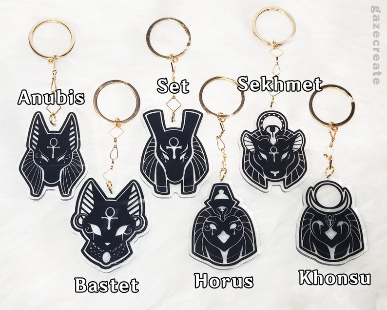 May include: Set of eight black and white Egyptian deity keychains with gold rings. The keychains feature Anubis, Set, Sekhmet, Bastet, Horus, Khonsu, and two other deities.