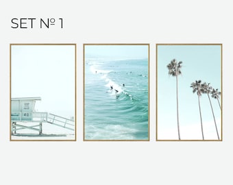 May include: A set of three framed prints featuring beach scenes. The first print shows a lifeguard stand on a sandy beach. The second print shows surfers riding waves in the ocean. The third print shows palm trees against a blue sky.