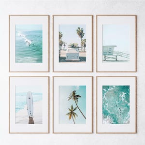 May include: A set of six framed prints featuring beach scenes, including surfers, a vintage van, palm trees, and a lifeguard stand. The prints are all in a light blue and white color scheme.