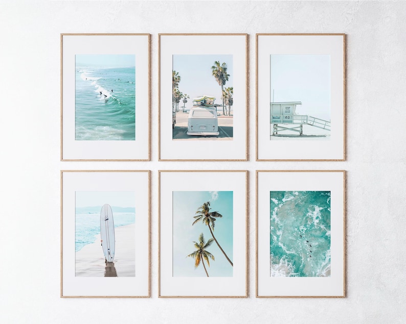 May include: A set of six framed prints featuring beach scenes, including surfers, a vintage van, palm trees, and a lifeguard stand. The prints are all in a light blue and white color scheme.