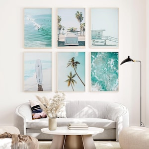 May include: A set of six framed prints featuring beach scenes. The prints include a surfboard, palm trees, a vintage van, a lifeguard stand, and ocean waves. The prints are arranged in a grid pattern on a white wall.