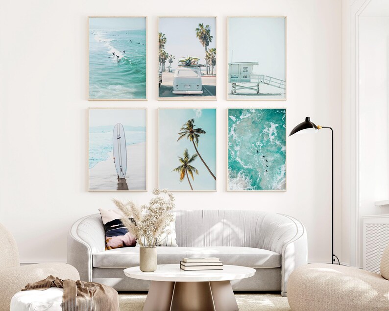 May include: A set of six framed prints featuring beach scenes. The prints include a surfboard, palm trees, a vintage van, a lifeguard stand, and ocean waves. The prints are arranged in a grid pattern on a white wall.