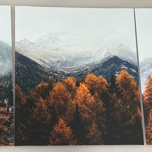 May include: A three-panel canvas print featuring a mountain landscape with snow-capped peaks and a forest of fall foliage in shades of orange, yellow, and brown.