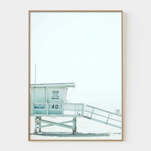 May include: A white lifeguard stand with a blue roof and a sign that reads "Lifeguard On Duty 911 Keep Off" and the number "40". The stand is on a sandy beach with a blue sky in the background.