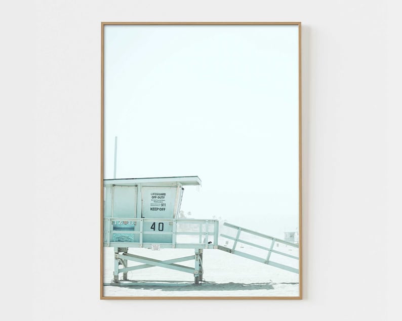 May include: A white lifeguard stand with a blue roof and a sign that reads "Lifeguard On Duty 911 Keep Off" and the number "40". The stand is on a sandy beach with a blue sky in the background.