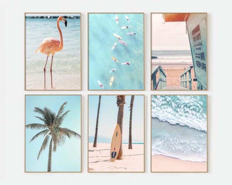 May include: A set of six framed prints featuring beach scenes. The prints include a pink flamingo standing on a beach, an aerial view of surfers in the ocean, a lifeguard stand on a beach, a palm tree on a beach, a surfboard leaning against a palm tree on a beach, and a close-up of ocean waves crashing on a beach.