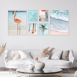 May include: A set of five framed prints featuring beach scenes. The prints include a pink flamingo standing in the water, a surfboard on the beach, a palm tree, a view of the ocean from above, and a wave crashing on the shore.