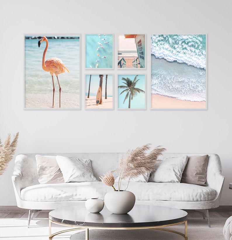 May include: A set of five framed prints featuring beach scenes. The prints include a pink flamingo standing in the water, a surfboard on the beach, a palm tree, a view of the ocean from above, and a wave crashing on the shore.
