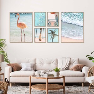 May include: A set of six framed prints featuring beach scenes. The prints include a pink flamingo standing in the water, a palm tree, a surfboard, a group of people swimming in the ocean, a lifeguard stand, and a wave crashing on the shore.