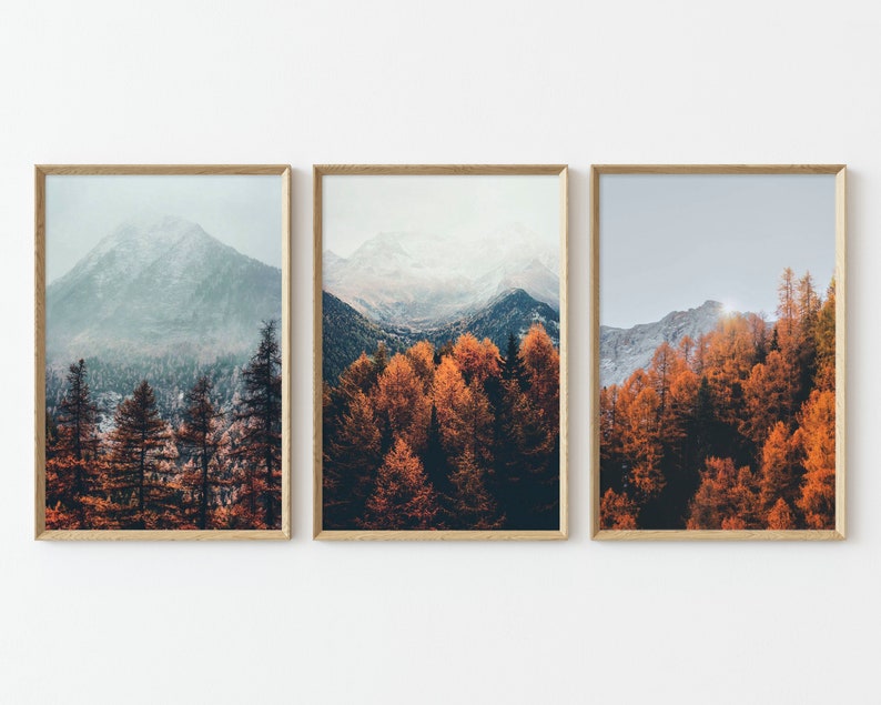 May include: Three framed prints of a mountain landscape with fall foliage. The left print shows a snow-capped mountain peak with a misty forest in the foreground. The middle print shows a forest of orange and red trees. The right print shows a mountain range with a forest of orange and red trees in the foreground.