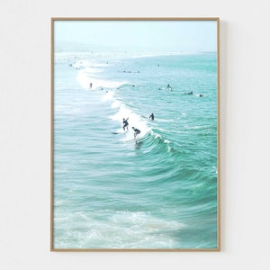 May include: A photograph of surfers riding waves in the ocean. The water is a vibrant turquoise color and the sky is a light blue. The surfers are silhouetted against the bright sky.