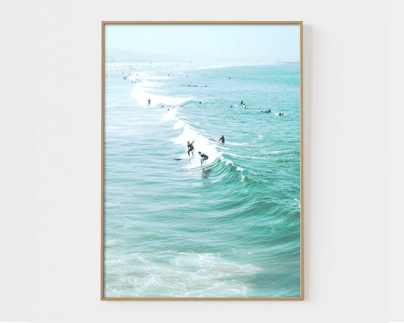 May include: A photograph of surfers riding waves in the ocean. The water is a vibrant turquoise color and the sky is a light blue. The surfers are silhouetted against the bright sky.