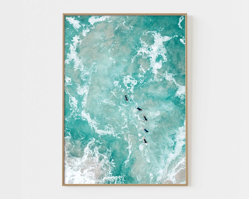 May include: An aerial view of turquoise ocean water with white foamy waves. Five people are swimming in the water, facing the camera.