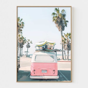 May include: A pink vintage van with surfboards on the roof parked on a beach with palm trees in the background.
