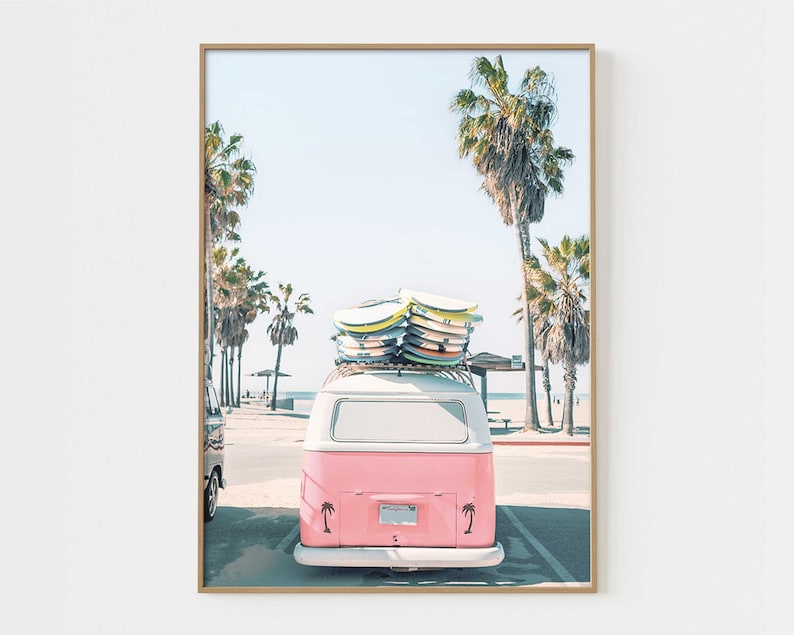 May include: A pink vintage van with surfboards on the roof parked on a beach with palm trees in the background.