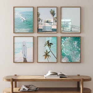 May include: Six framed prints of beach scenes, including a surfboard, palm trees, a lifeguard stand, and a vintage van. The prints are arranged in a grid on a light wood wall.