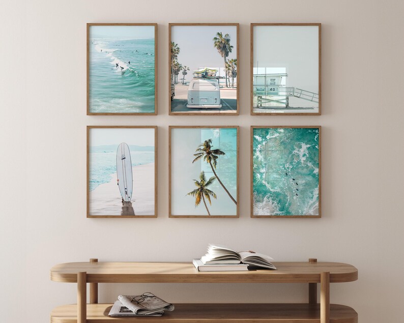 May include: Six framed prints of beach scenes, including a surfboard, palm trees, a lifeguard stand, and a vintage van. The prints are arranged in a grid on a light wood wall.