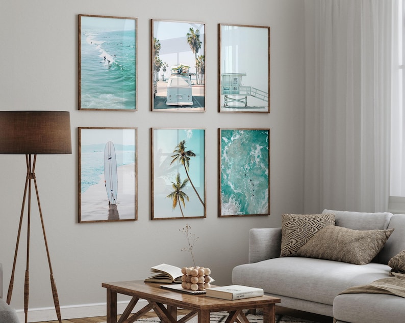 May include: A set of six framed prints featuring beach scenes. The prints include a surfboard on the beach, palm trees, a vintage van, and ocean waves. The prints are all in a light blue and green color scheme.