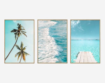 May include: Three framed prints of tropical beach scenes. The first print shows two palm trees against a blue sky. The second print shows a close-up of ocean waves. The third print shows a wooden dock extending into a turquoise lagoon.
