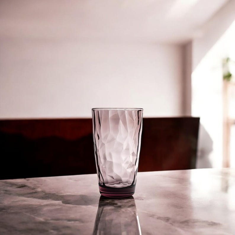 Puede incluir: Un vaso alto de color morado transl&uacute;cido con una textura superficial geom&eacute;trica y facetada. El vaso tiene una forma cil&iacute;ndrica con un borde ligeramente m&aacute;s ancho y una base plana y s&oacute;lida, reflejando la luz a trav&eacute;s de su exterior angular.