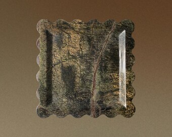 May include: A square stone tray featuring a dark green and brown marbled pattern with natural veining. The tray has a distinct scalloped edge design on all four sides, creating a wavy border around the flat, polished surface of the stone.
