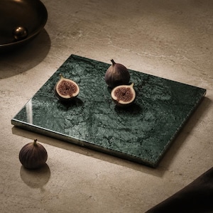 May include: A rectangular dark green marble serving board with a polished finish and natural veining. The board is displayed with three fresh figs, including one whole fig placed off the board and two halved figs resting on the marble surface.